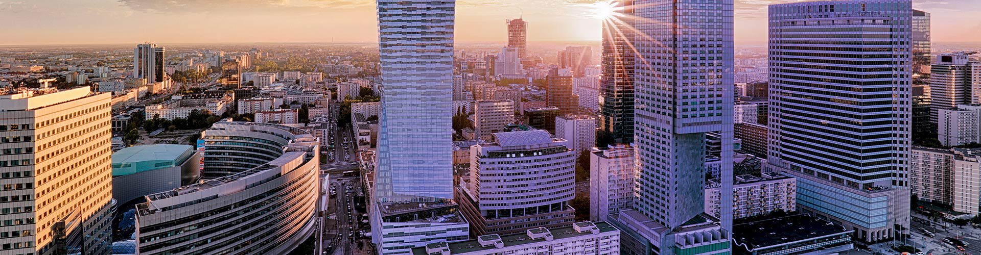 Panoramic aerial view of Warsaw, Poland, at sunset, featuring modern skyscrapers, busy streets, and the city skyline.