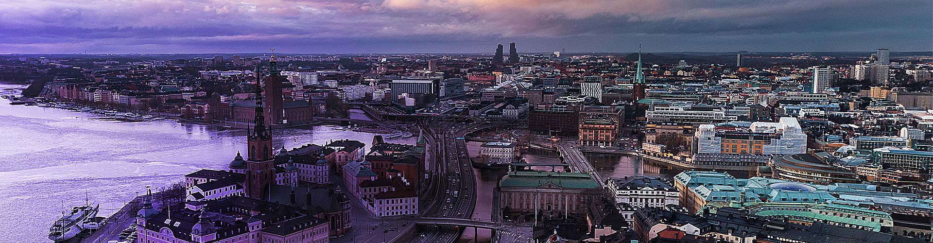 Aerial view of Stockholm, Sweden, with waterways, historic spires, and city buildings under a dramatic twilight sky.