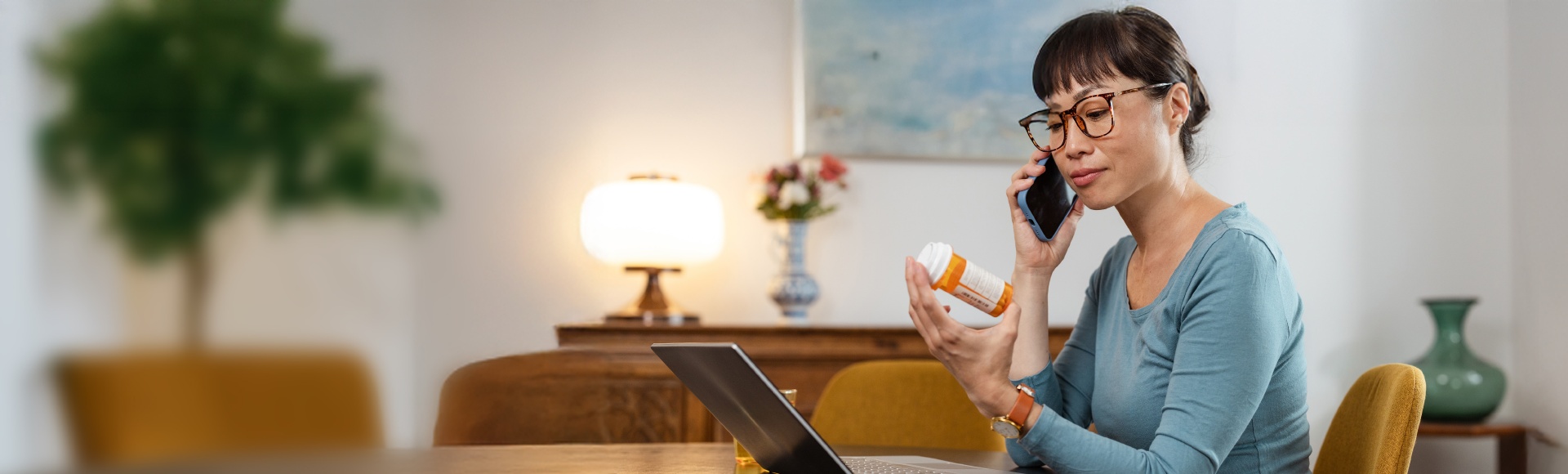 TP employee reviewing medication while on a phone call at a home workspace.