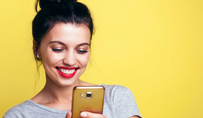 Woman smiling while looking at her phone against a yellow background.