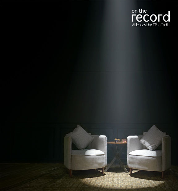 Studio with two armchairs and a small table on a rug under spotlight; dark paneled wall background.