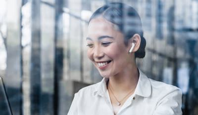 Smiling Asian professional working on her laptop inside a modern glass-walled coworking space.