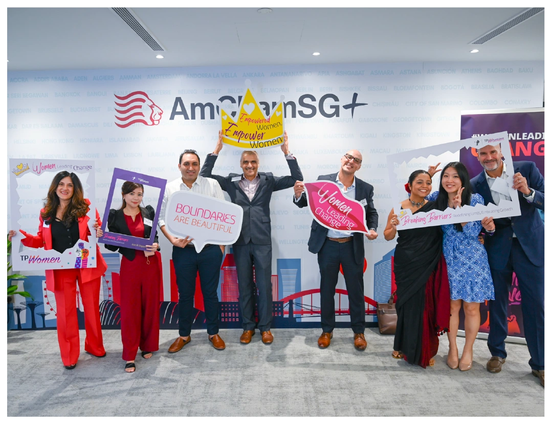 A diverse group poses with signs celebrating women’s empowerment at AmChamSG+.