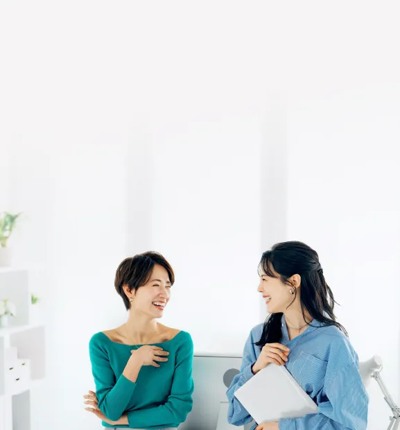 Two smiling professional women converse in a bright office.