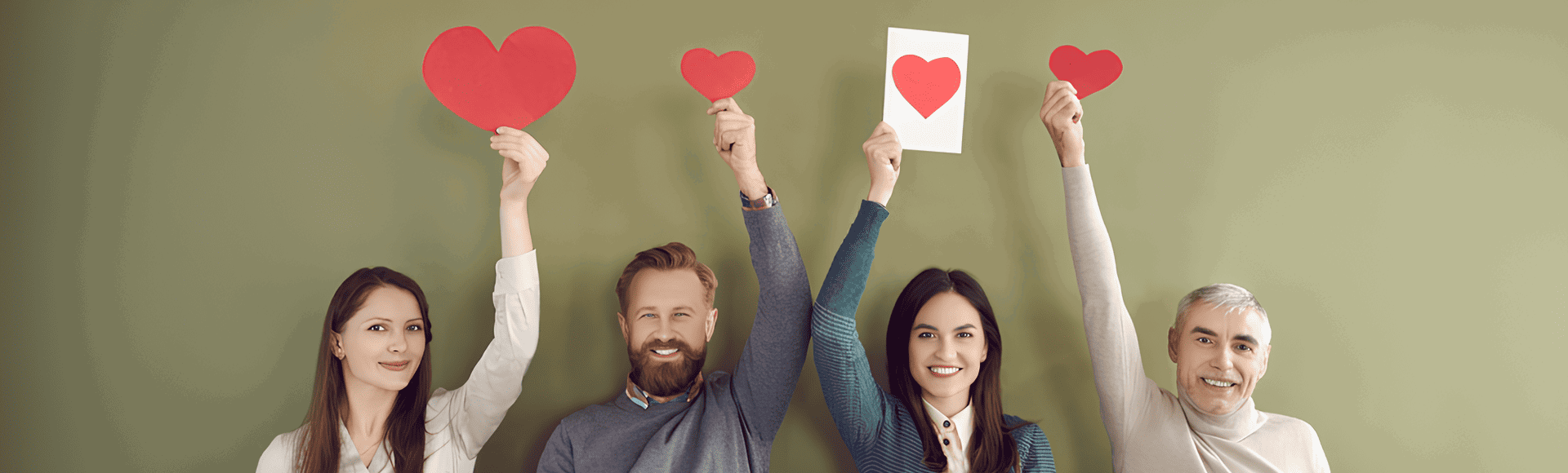 Group of smiling people holding up red paper hearts against a green background.