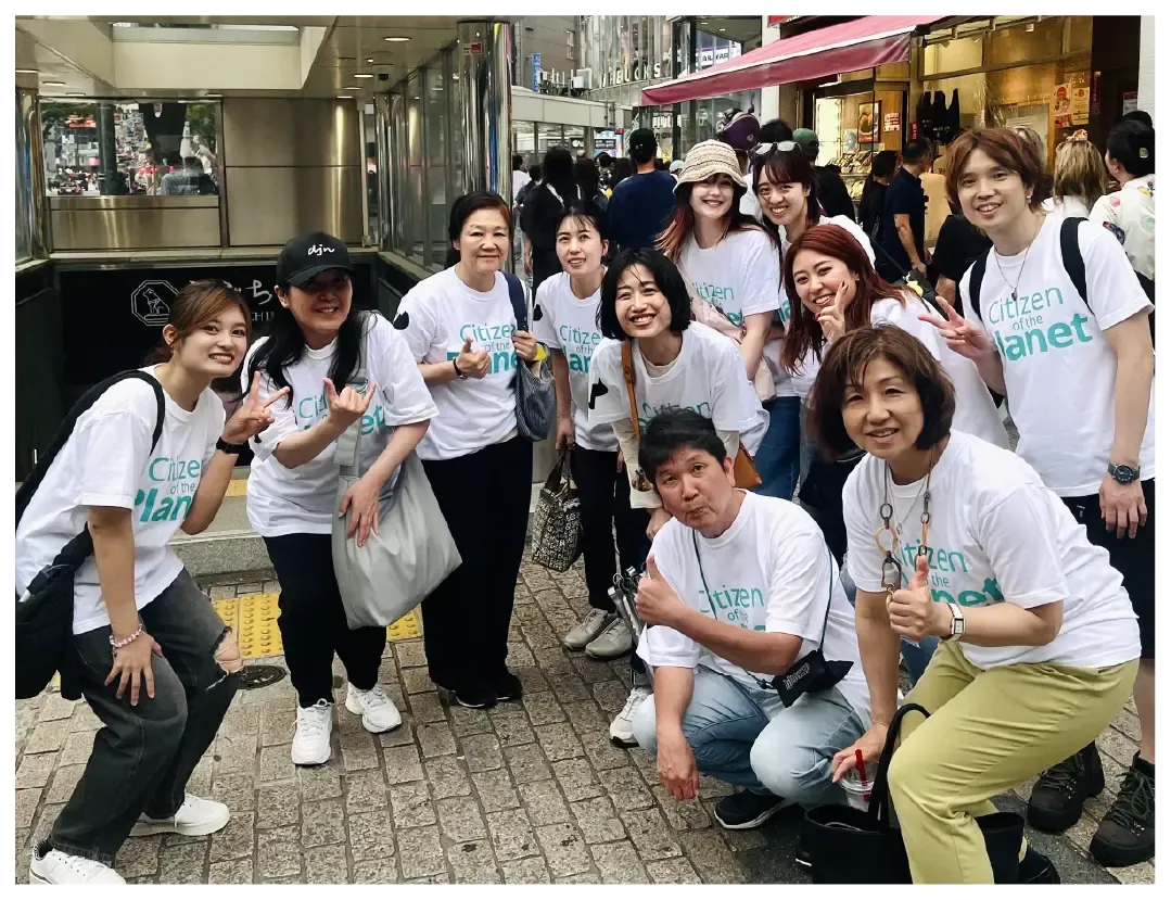 A group of people in matching "Citizen of the Planet" shirts pose on a city street.