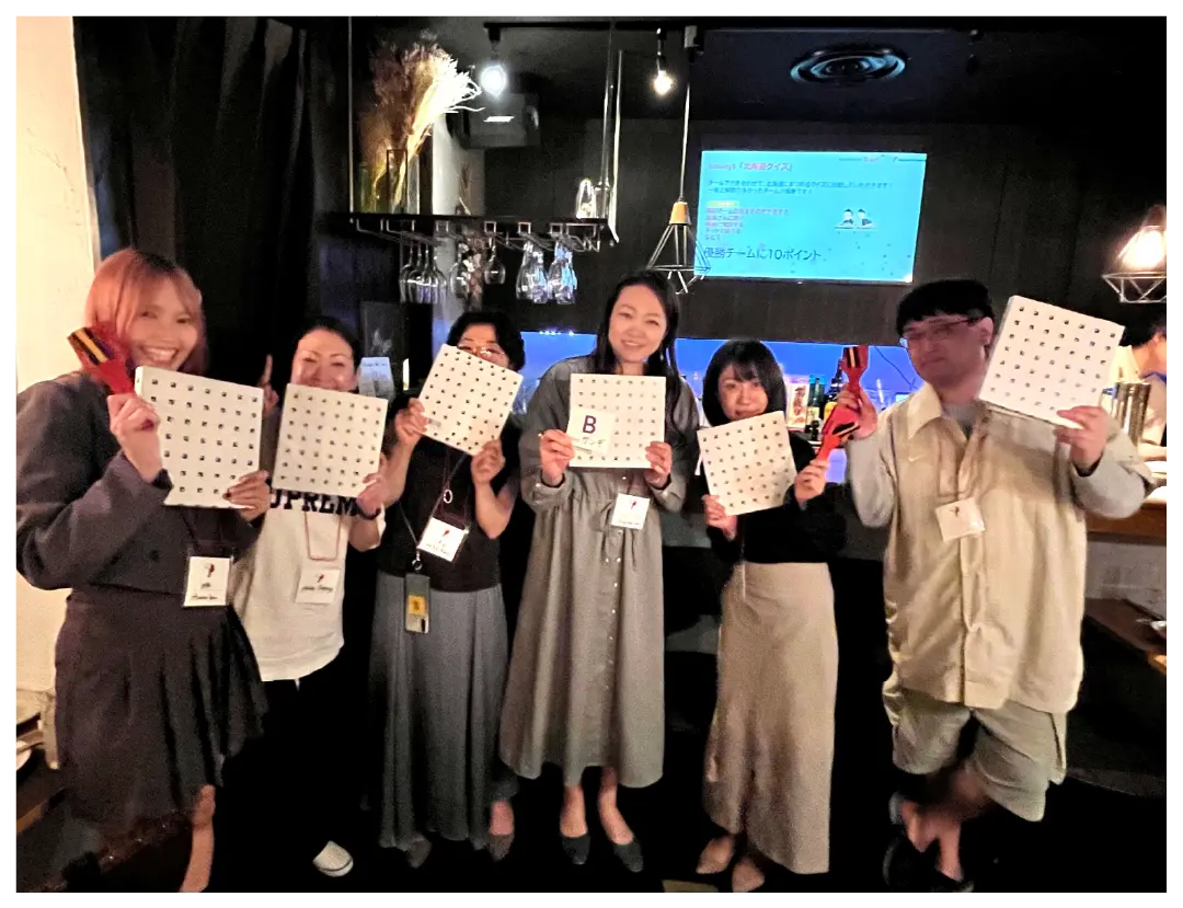 Six people smile and pose with prizes at a lively indoor event.