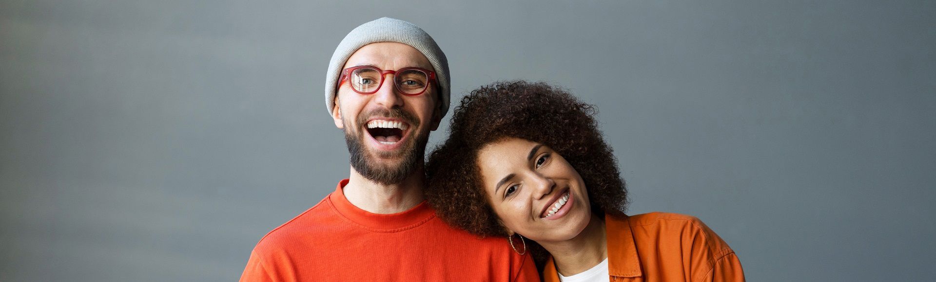 Smiling colleagues in red outfits, with the woman resting her head on her coworker’s shoulder.
