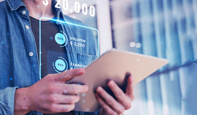 A person uses a tablet while interacting with a holographic financial interface displaying income, expenses, and a fluctuating data graph.