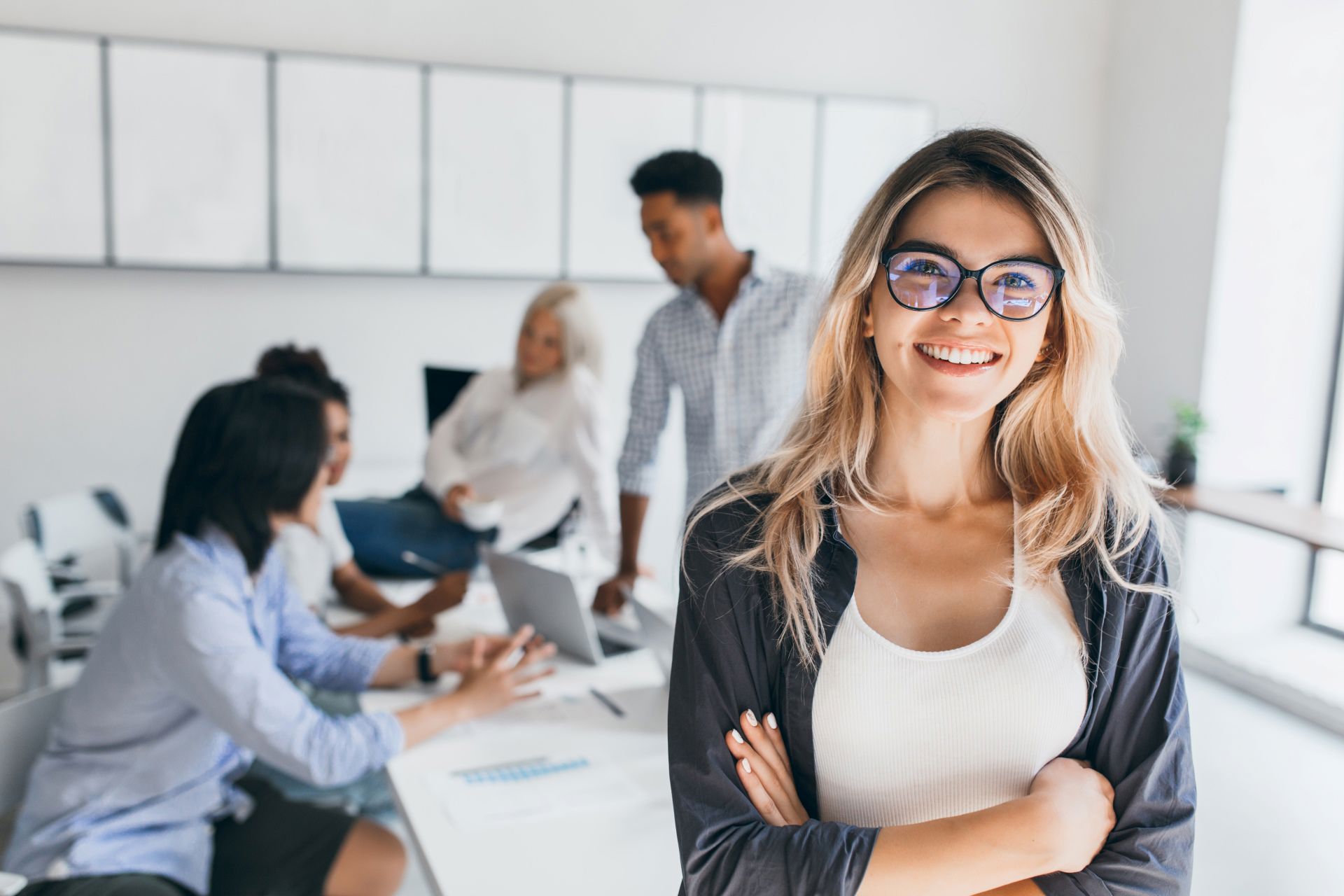 Business woman crossing arms and smiling at camera during a meeting with her team  