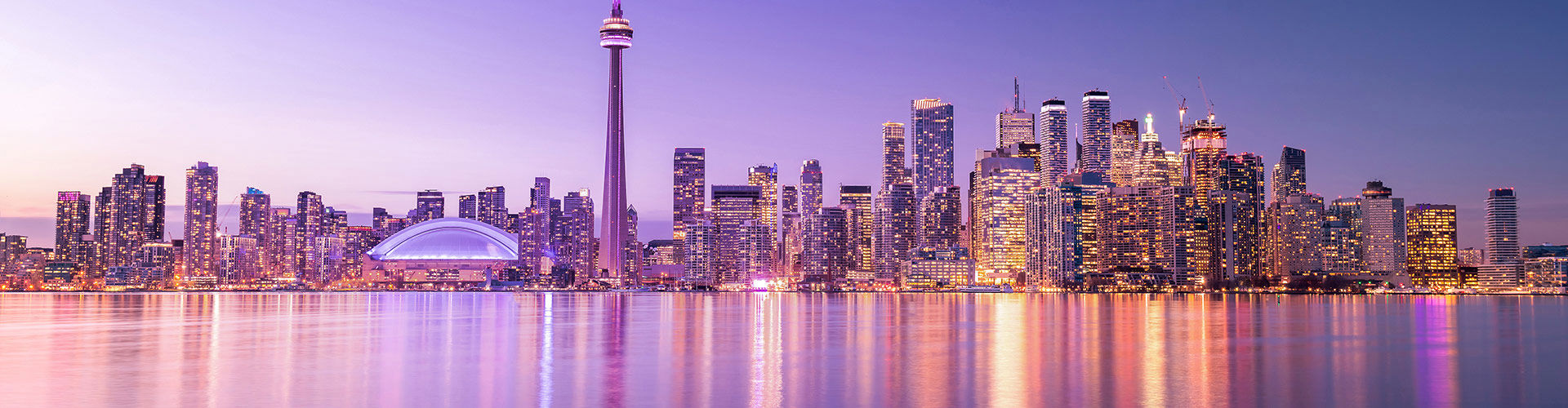 Toronto skyline with the CN Tower at sunset, viewed across the waterfront.
