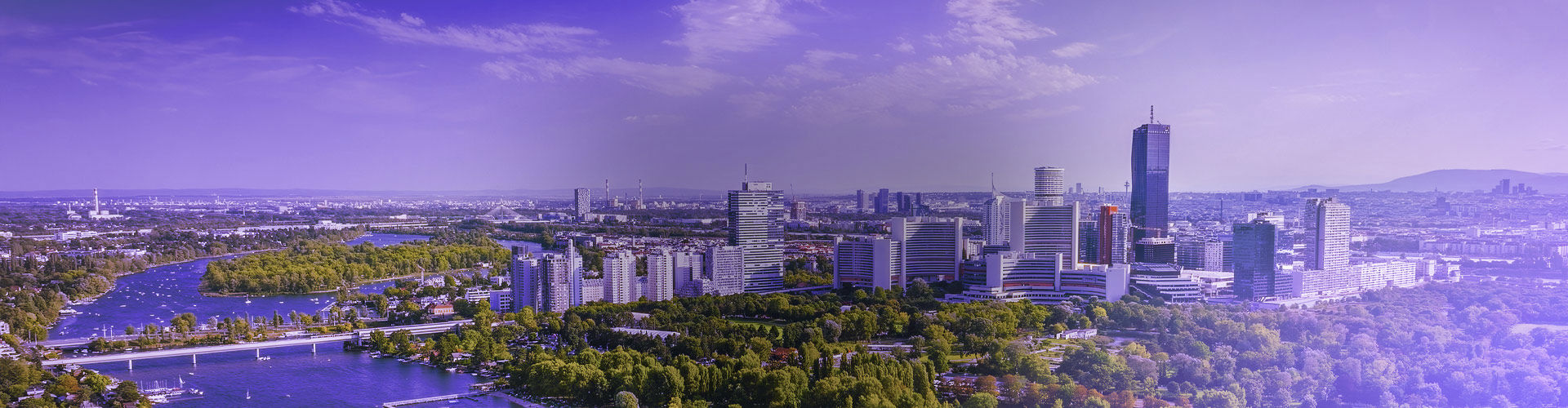 Panoramic aerial view of Vienna, Austria, featuring the modern city skyline, the Danube River, bridges, and lush green parks.