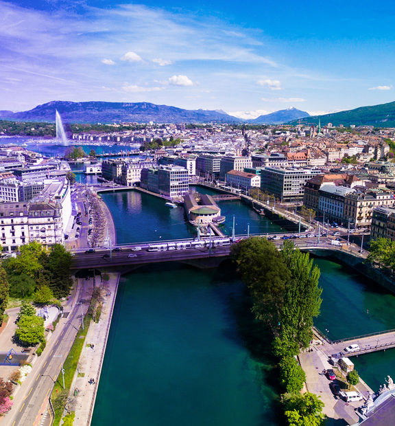 Geneva cityscape with Lake Geneva, bridges, and surrounding mountains.