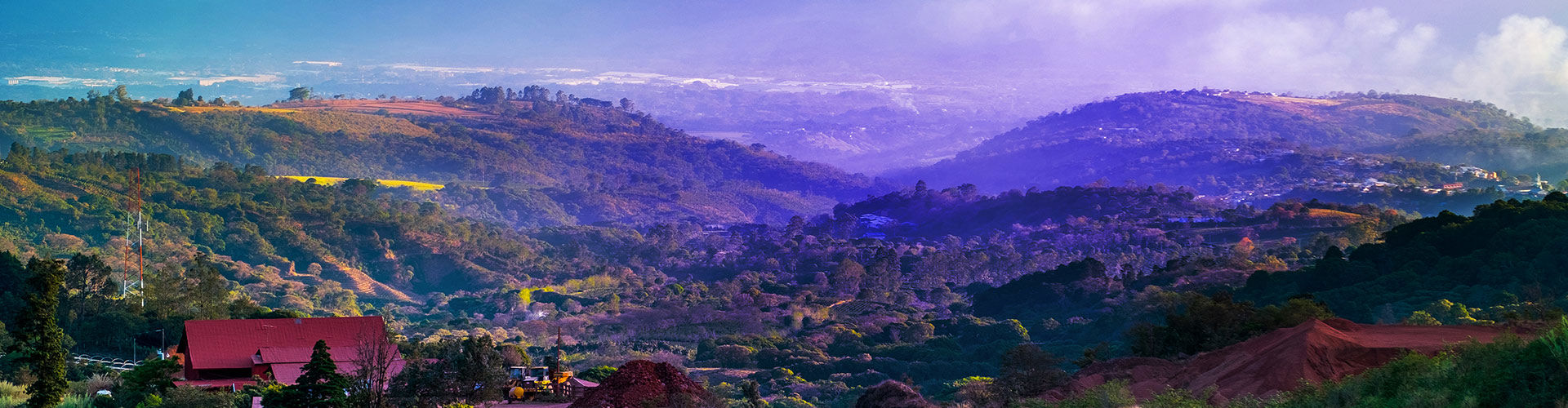 Panoramic view of Costa Rica’s lush mountainous landscape, with rolling green hills, dense vegetation, agricultural fields, and misty valleys beneath a cloudy sky.