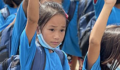 Children in blue school uniforms raising their hands during a classroom activity.