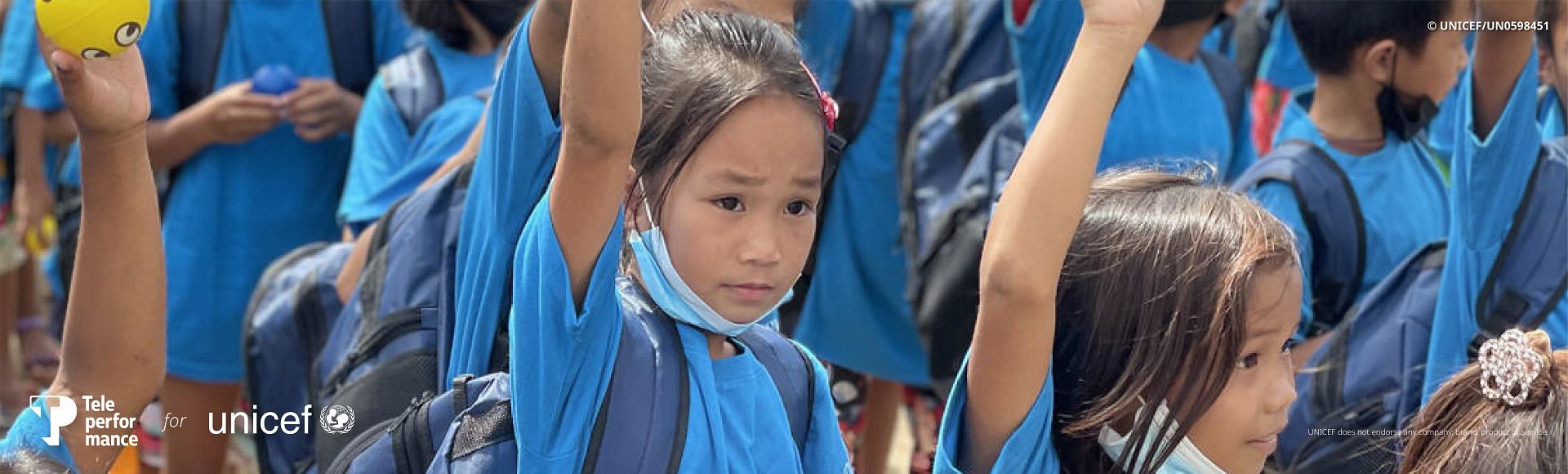 Children in blue school uniforms raising their hands during a classroom activity.