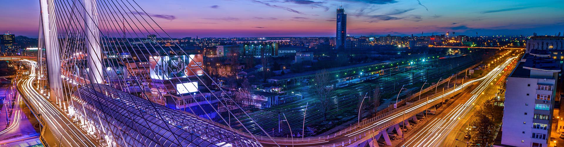 Bucharest cityscape at dusk with a cable-stayed bridge and illuminated roads.