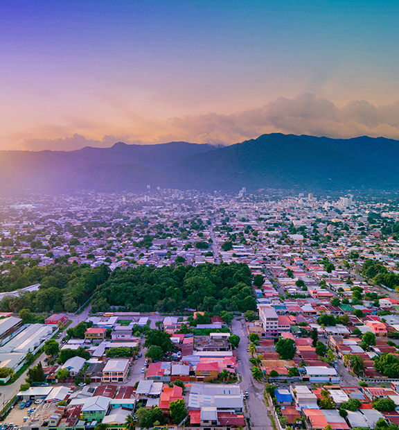 Panoramic view of Tegucigalpa, Honduras, at sunset, featuring a sprawling urban landscape surrounded by lush green mountains.