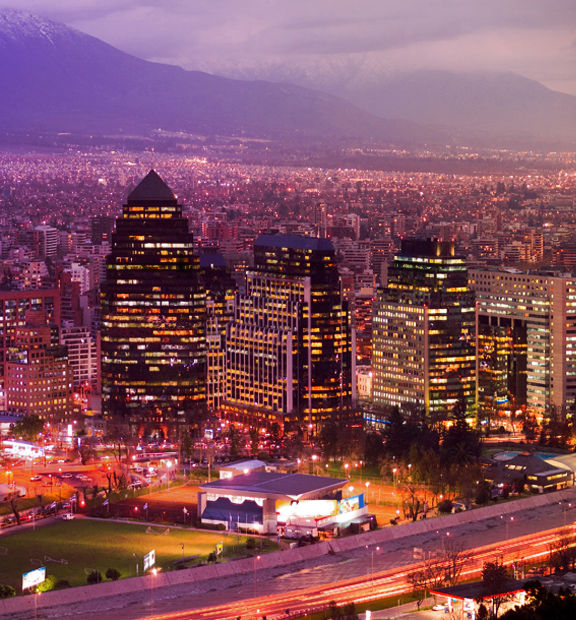 Panoramic nighttime view of Santiago, Chile, with illuminated skyscrapers and a dense cityscape stretching toward the horizon.