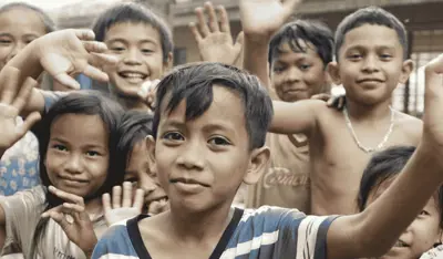 Children supported by the TP and UNICEF partnership smiling and waving at the camera.