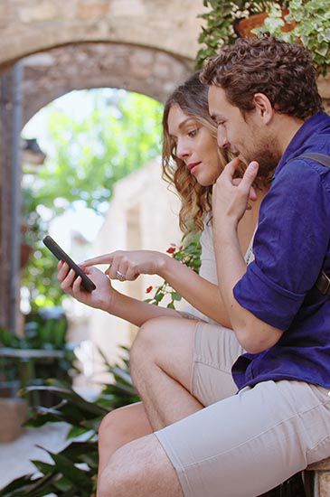 Una coppia è seduta su gradini di pietra, guardando con attenzione uno smartphone.