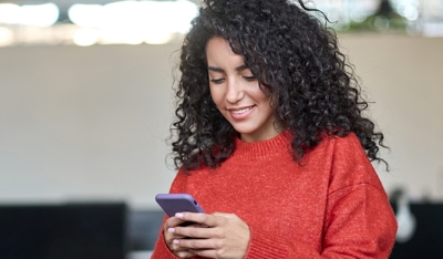 A young woman in a red blouse is using her smartphone.