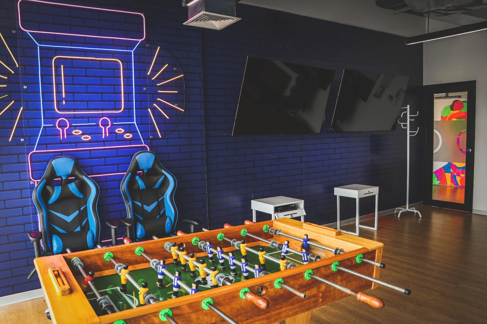 TP game room with gaming chairs, foosball table, neon wall art, and mounted TVs.
