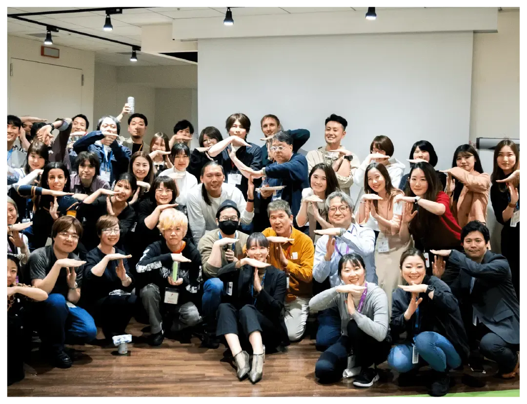 A large group of people pose playfully with matching hand gestures.