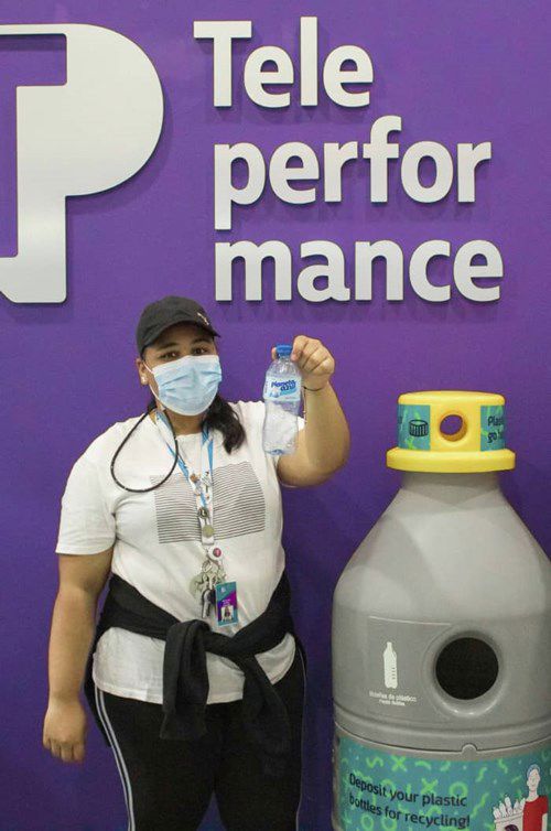Employee holding a plastic bottle for recycling next to a recycling container at TP.