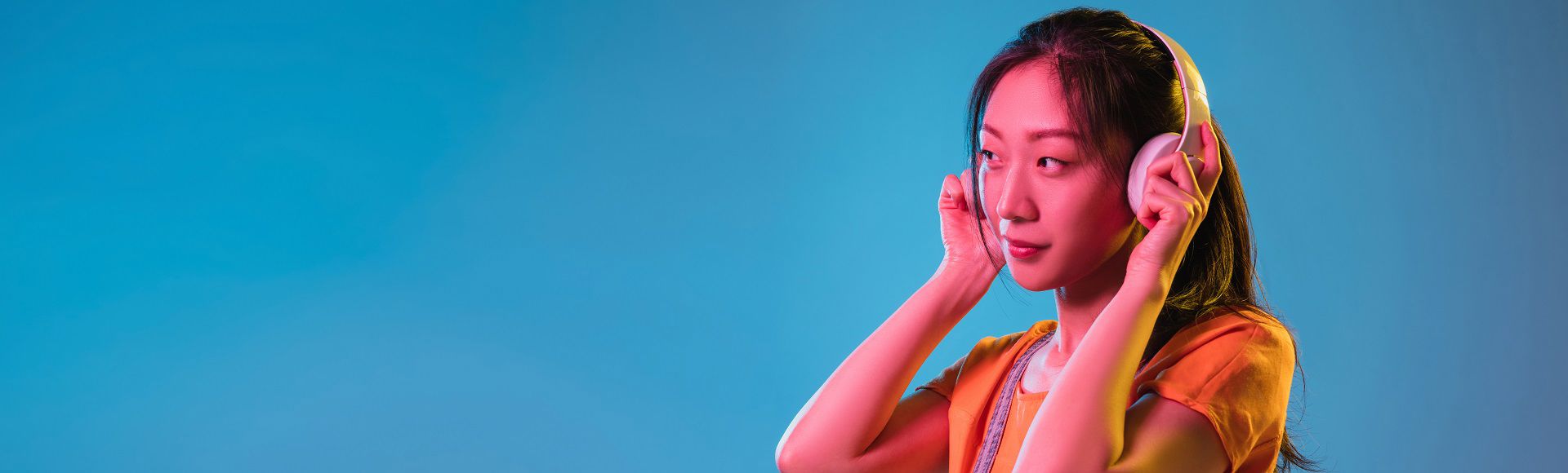 Woman wearing headphones and listening attentively against a blue background.