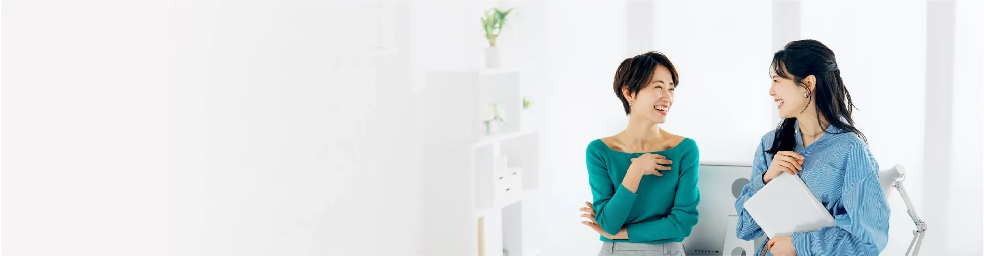 Two smiling professional women converse in a bright office.