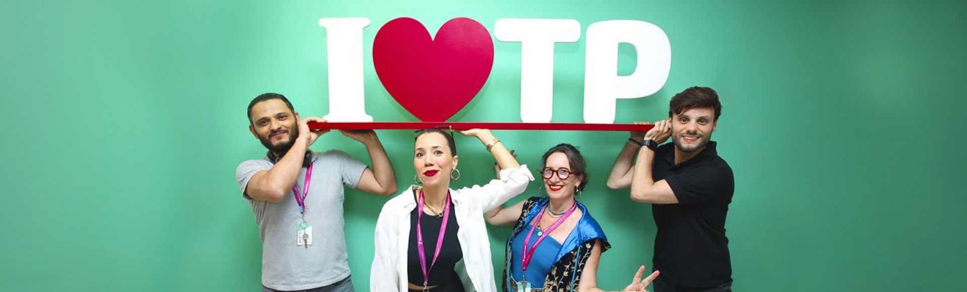 Employees smiling while holding an I love TP sign against a green background.
