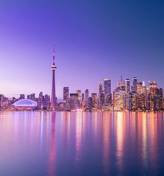 Toronto skyline with the CN Tower at sunset, viewed across the waterfront.
