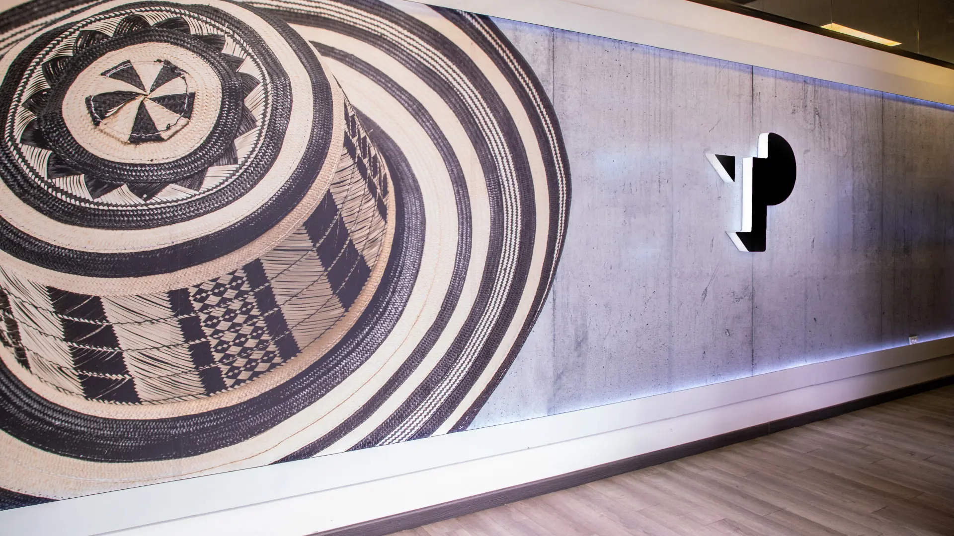 Wall with cultural artwork and illuminated TP logo in office space.
