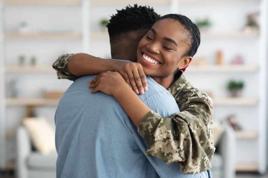 Black woman in military uniform sharing a warm embrace with a loved one.