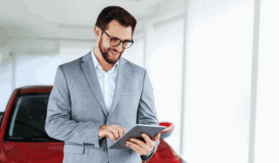 A man in an elegant suit uses a tablet in front of a car, reflecting luxury and innovation. 