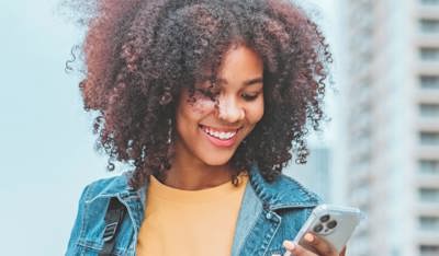 Smiling girl checking her mobile phone on the street.