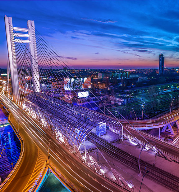 Bucharest cityscape at dusk with a cable-stayed bridge and illuminated roads.