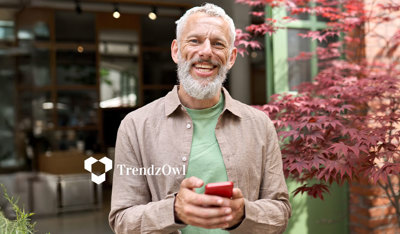 Smiling senior man holding his smartphone with flowers in the background, illustrating healthcare.
