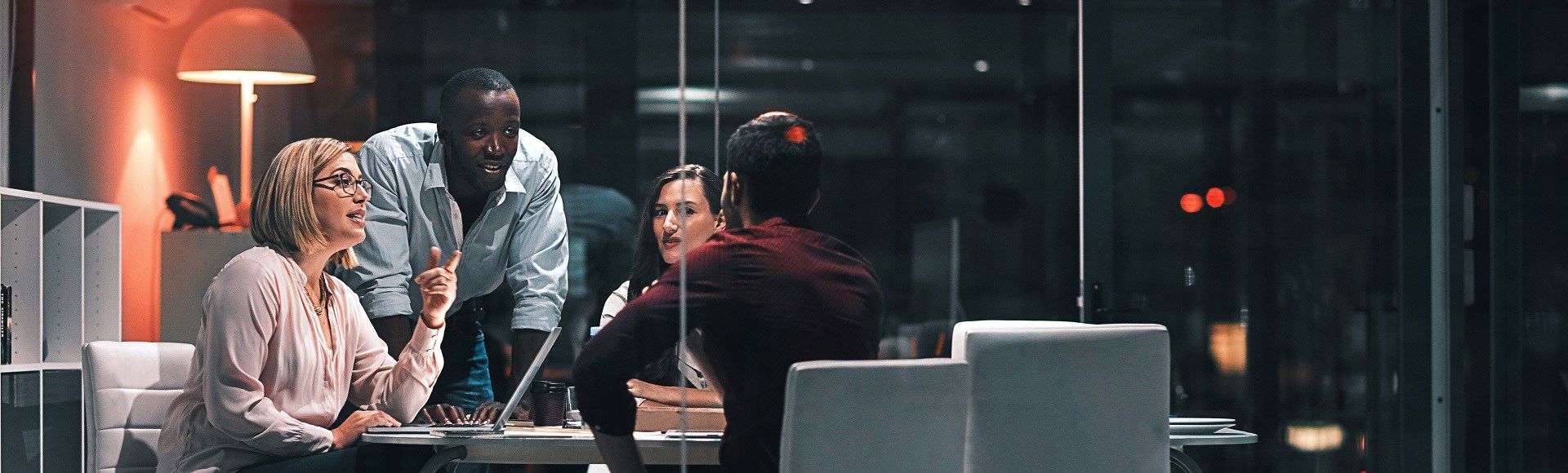 Group of four diverse professionals having a late-night meeting in a modern office.