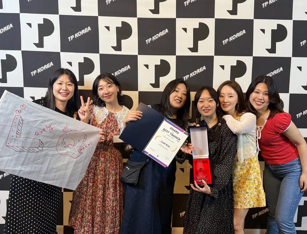 A group of colleagues celebrate a team member winning the "Best Trainer" award.