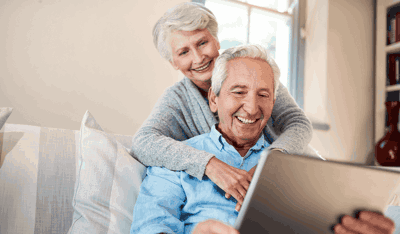 Smiling elderly couple sitting on a sofa while looking at a tablet.