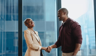 Two professionals smiling and shaking hands in a modern office with large glass windows