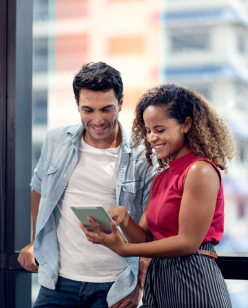 Two colleagues smiling and reviewing content on a tablet in a professional setting.