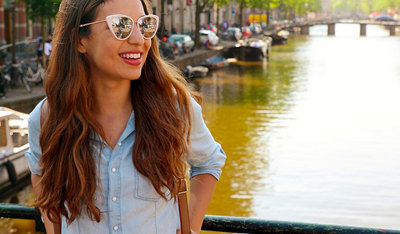 Smiling woman with backpack standing by a canal in a European city.