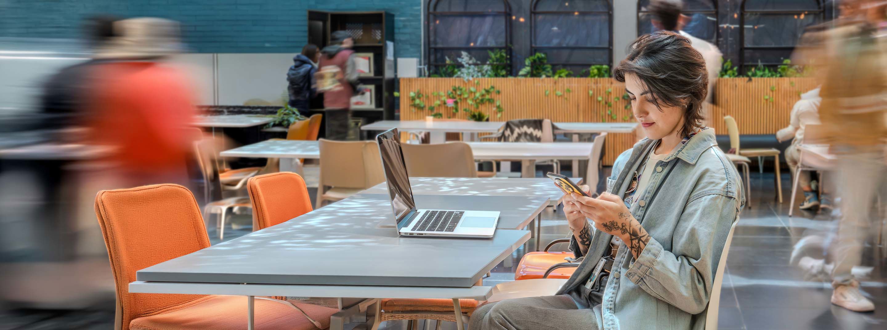Woman using a smartphone beside a laptop in a modern workspace.