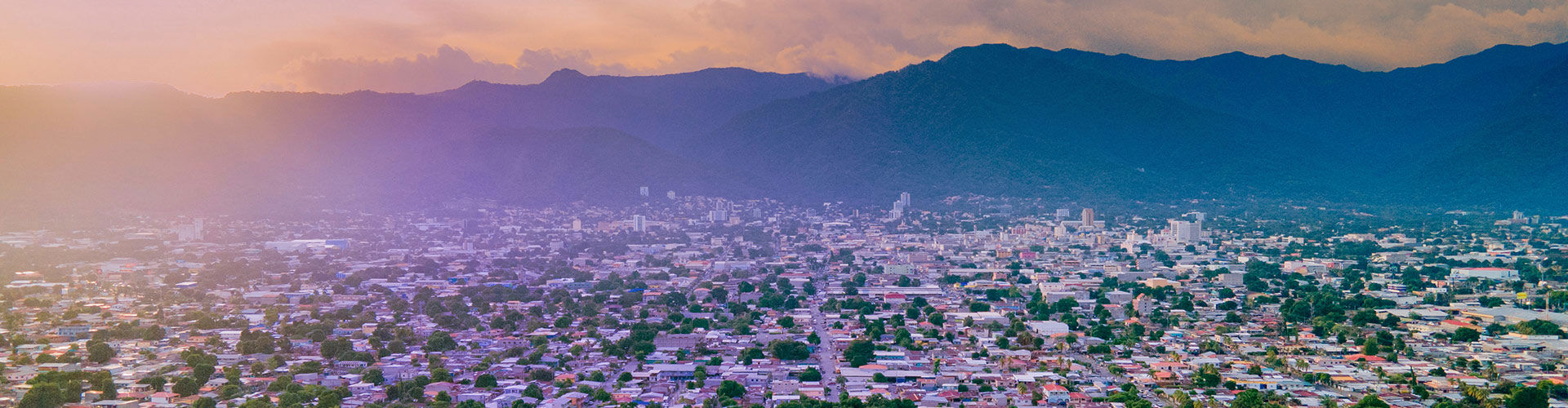 Panoramic view of Tegucigalpa, Honduras, at sunset, featuring a sprawling urban landscape surrounded by lush green mountains.