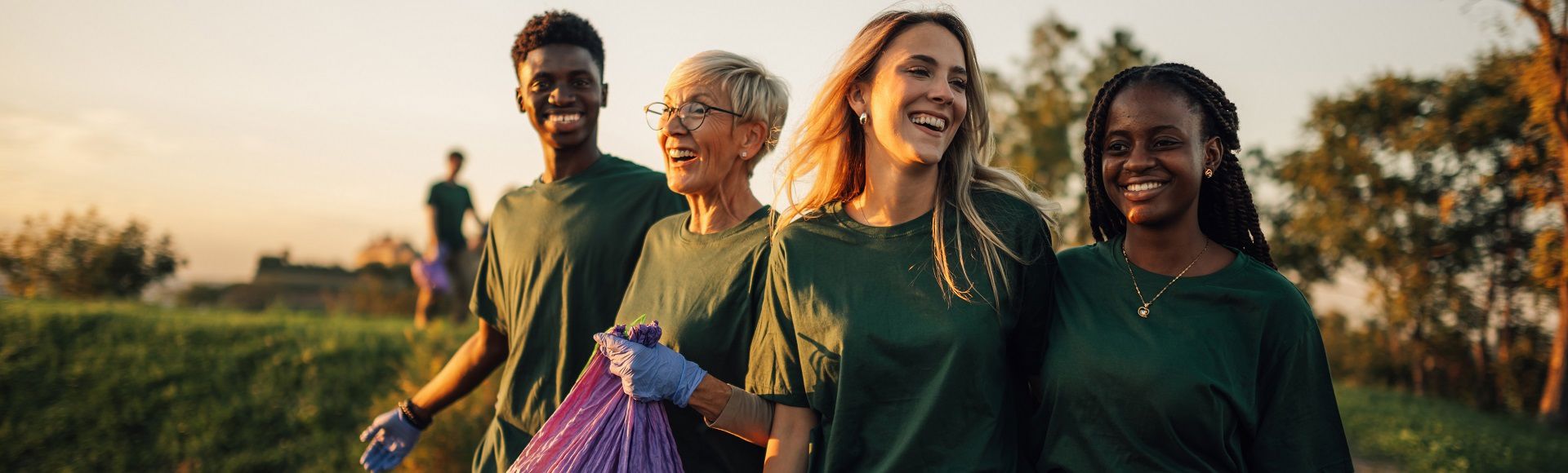 Group of volunteers smiling while collecting litter outdoors at sunset.