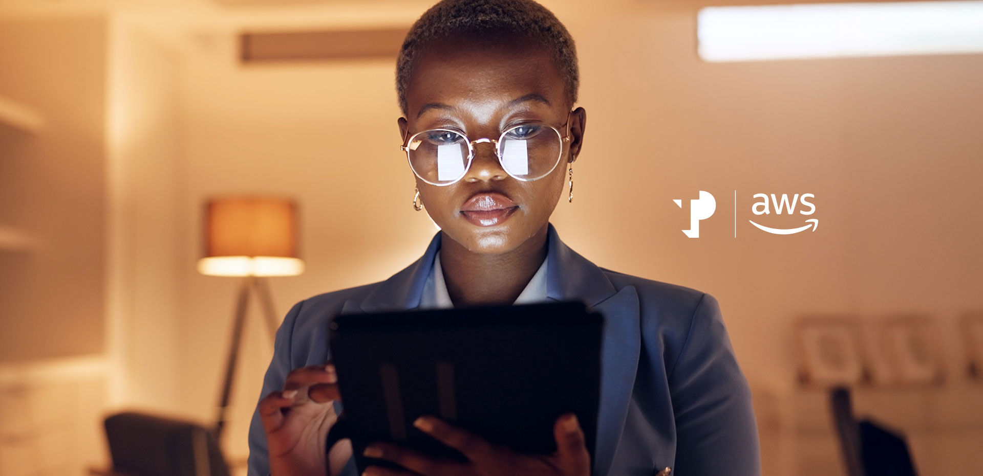 A person with glasses reads a tablet in a warmly lit room with a floor lamp.