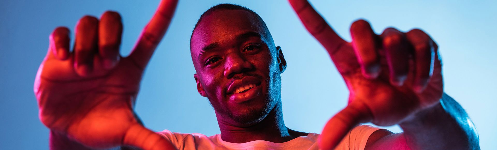 Smiling man framing the camera with his hands against a colorful background.
